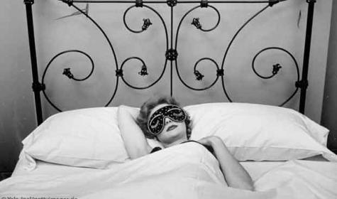 Frau mit Schlafmaske in schmiedeeisernem Bett