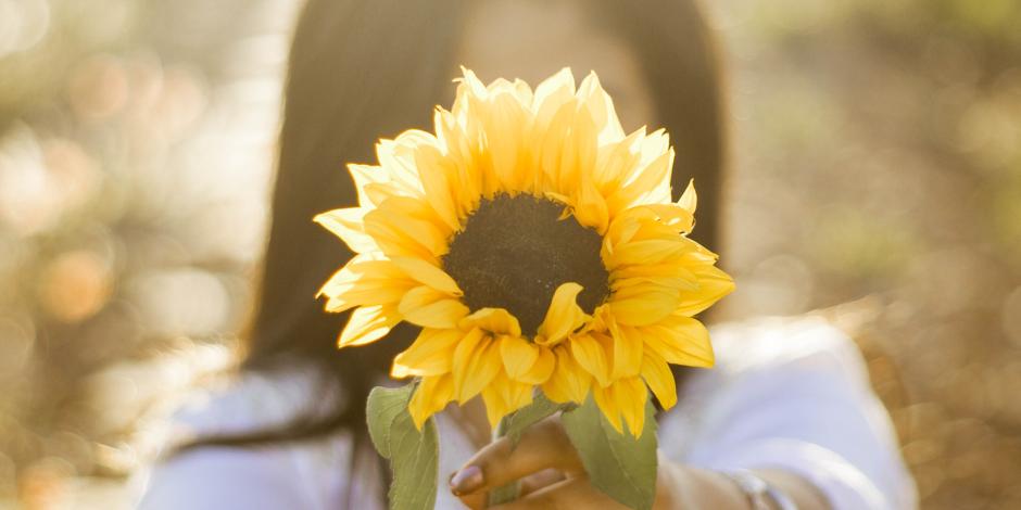 woman holding a sunflower to the camera