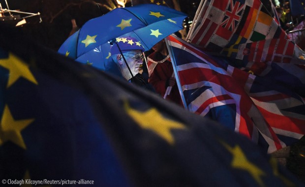 An anti-Brexit protester stands with an illuminated EU umbrella surrounded in flags outside the Houses of Parliament in London