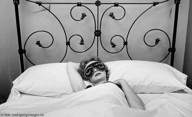 Frau mit Schlafmaske in schmiedeeisernem Bett