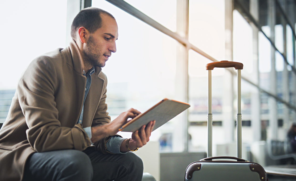 Mann liest am Flughafen auf seinem Tablet englischen Text