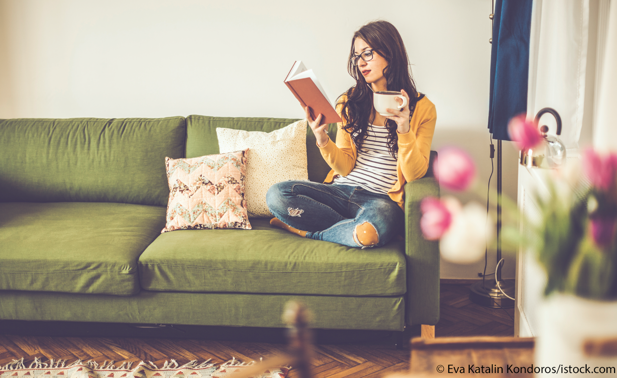 Frau liest einen englischen Text (Roman) auf dem Sofa