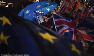 An anti-Brexit protester stands with an illuminated EU umbrella surrounded in flags outside the Houses of Parliament in London