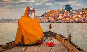 Sadhu baba in meditation on a wooden boat overlooking the historic Varanasi city and Ganges river ghats, India.
