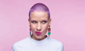  Thoughtful young woman wearing white t-shirt and funny lollipops earrings looking away. Studio portrait on pink background.
