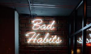 A neon sign saying "bad habits" against a dark backdrop