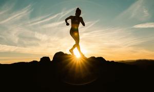 woman running across jagged rock with sun in the background