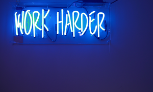 blue neon sign saying "work harder"