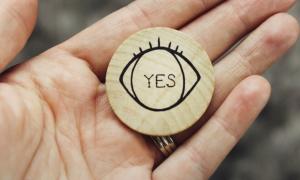 a hand holding a wooden coin with "yes" written on it