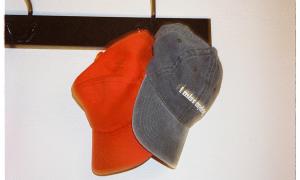 A pair of casual caps hang on a hook on a wall; one reads "I miss my dog"