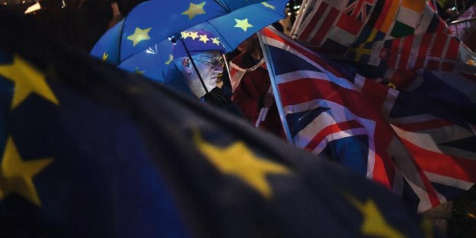 An anti-Brexit protester stands with an illuminated EU umbrella surrounded in flags outside the Houses of Parliament in London