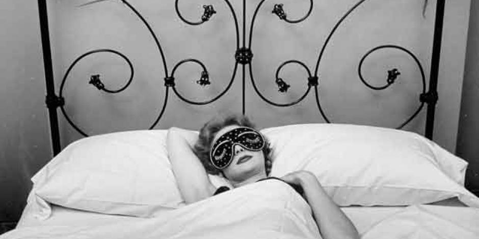 Frau mit Schlafmaske in schmiedeeisernem Bett