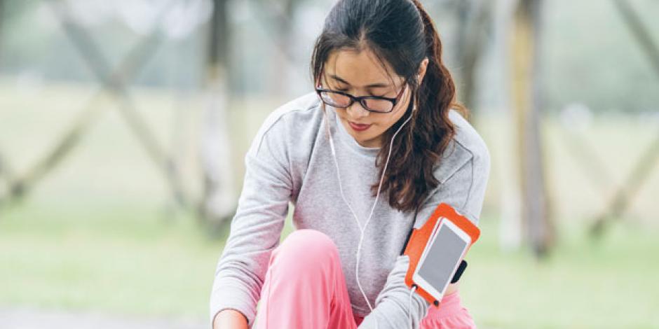 Frau mit Fitnesstracker schnürt sich die Schuhe zu