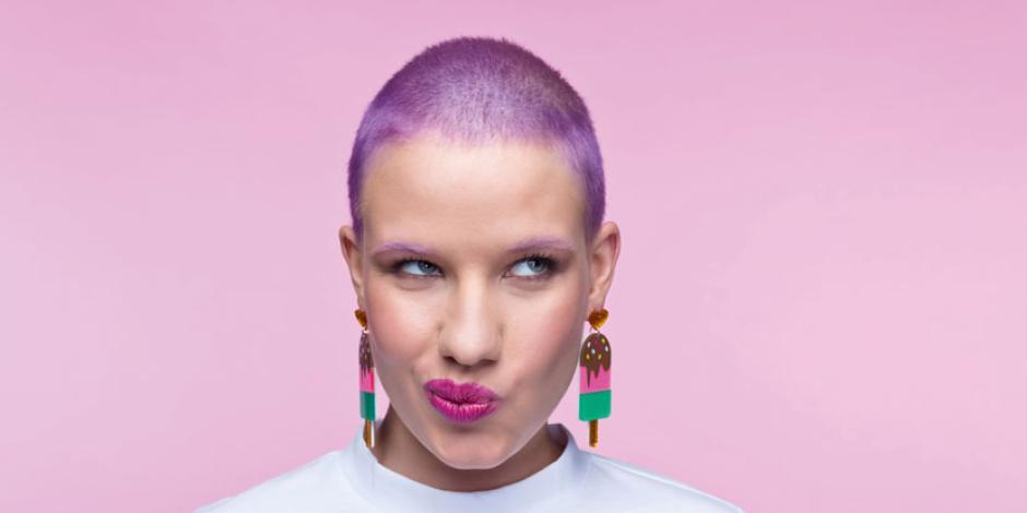  Thoughtful young woman wearing white t-shirt and funny lollipops earrings looking away. Studio portrait on pink background.