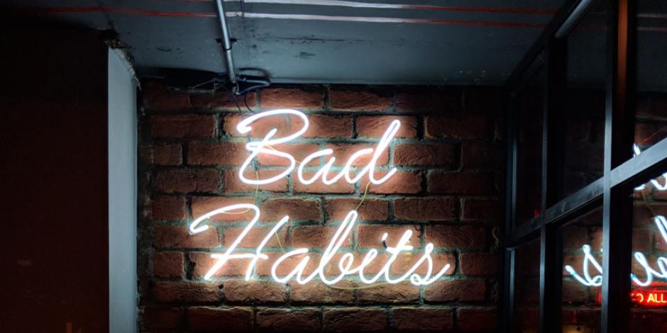 A neon sign saying "bad habits" against a dark backdrop