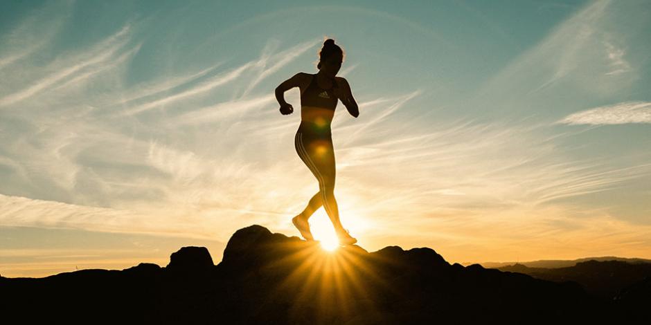 woman running across jagged rock with sun in the background