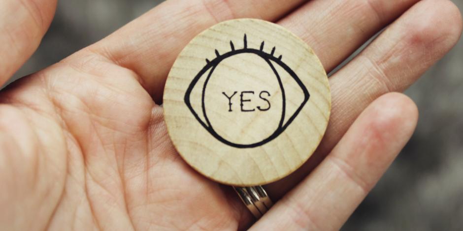 a hand holding a wooden coin with "yes" written on it