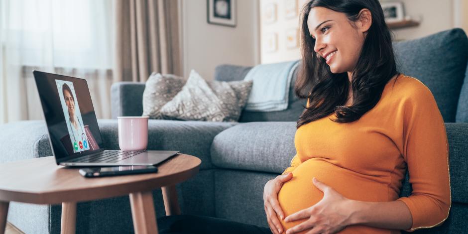 Young beautiful pregnant woman having video call with doctor using laptop at home