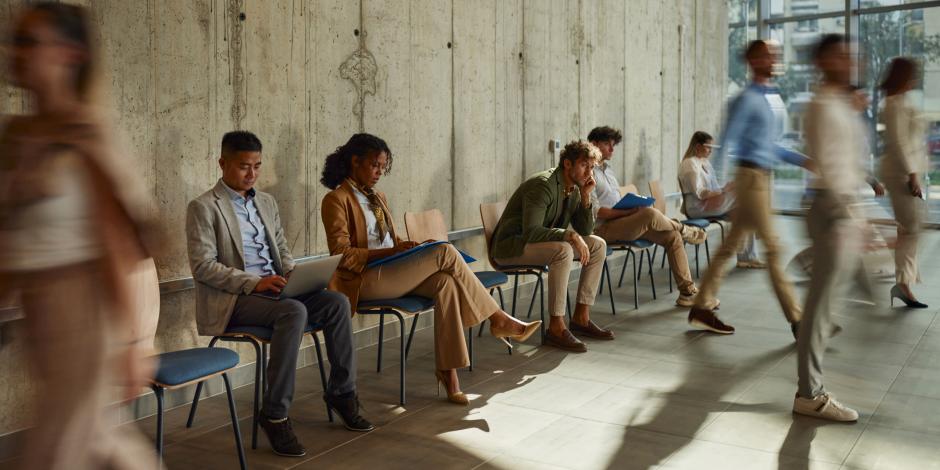 a row of professionally dressed applicants seated and standing near a concrete wall