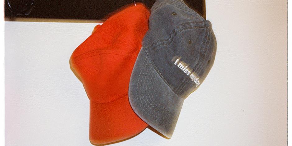 A pair of casual caps hang on a hook on a wall; one reads "I miss my dog"