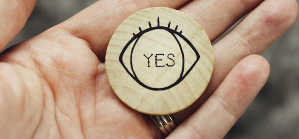 a hand holding a wooden coin with "yes" written on it