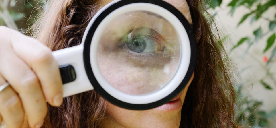 the giant eye of a girl looking at you from behind a magnifying glass