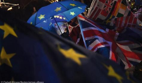 An anti-Brexit protester stands with an illuminated EU umbrella surrounded in flags outside the Houses of Parliament in London
