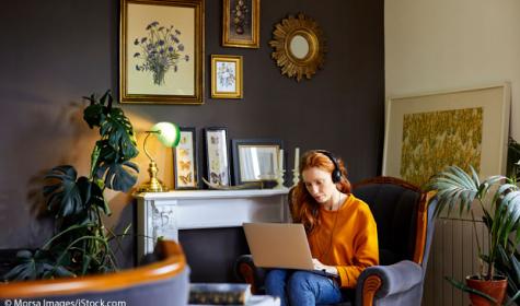 Frau sitzt mit Computer in ihrem Wohnzimmer