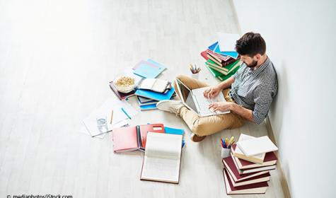 junger Mann beim Lesen englischer Texte inmitten eines Stapels von Büchern