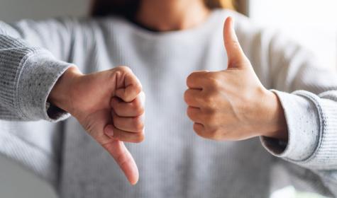 Close-up image of a woman with one thumb up and one thumb down