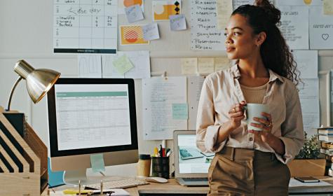 A woman in an office with a cup of coffee and lots of notes about upcoming projects