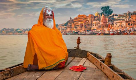 Sadhu baba in meditation on a wooden boat overlooking the historic Varanasi city and Ganges river ghats, India.