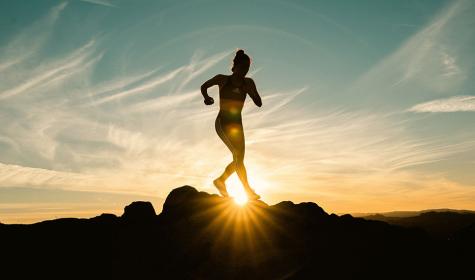 woman running across jagged rock with sun in the background