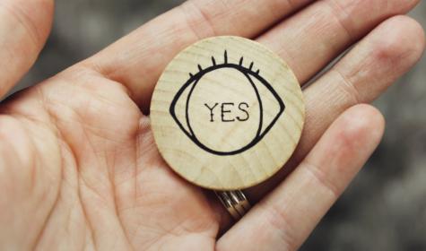a hand holding a wooden coin with "yes" written on it