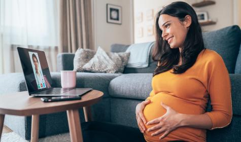 Young beautiful pregnant woman having video call with doctor using laptop at home