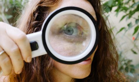 the giant eye of a girl looking at you from behind a magnifying glass