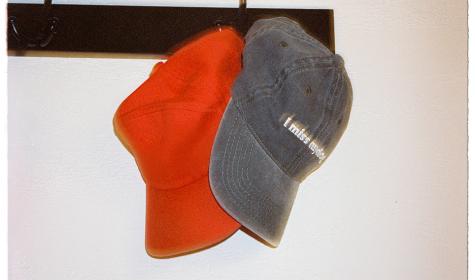 A pair of casual caps hang on a hook on a wall; one reads "I miss my dog"